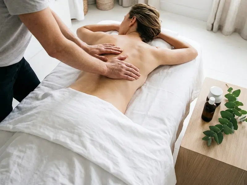 Oil massage — both hands working down the back, oil and eucalyptus on a side table